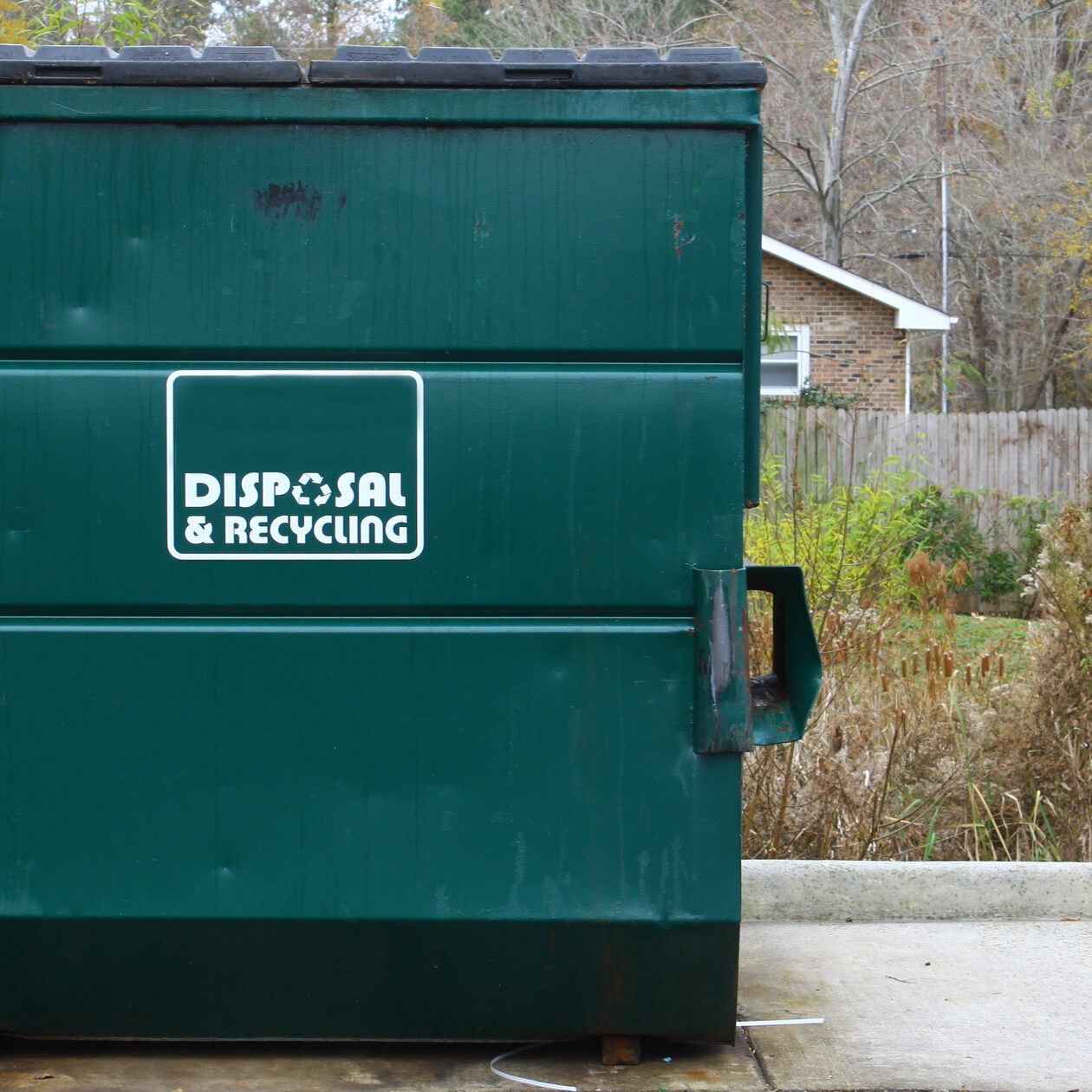 A large green disposal and recycling dumpster parked outside on a concrete slab